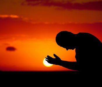 A man praying with hands open. Silhouette. Panoramic image of side view of Caucasian male praying with palms upward. Man is bowing down with ocean and dramatic sun behind. One person is in the image, taking in a tropical climate. Themes include spirituality, balance, lifestyle, salvation, praying, faith, meditation, contentment, vitality, wellness, hope, heaven, healing, deliverance, sin, struggle, help, and relationships.